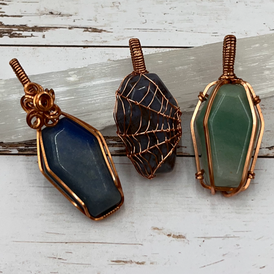 Three wire-wrapped, coffin shaped stone pendants on a wooden surface