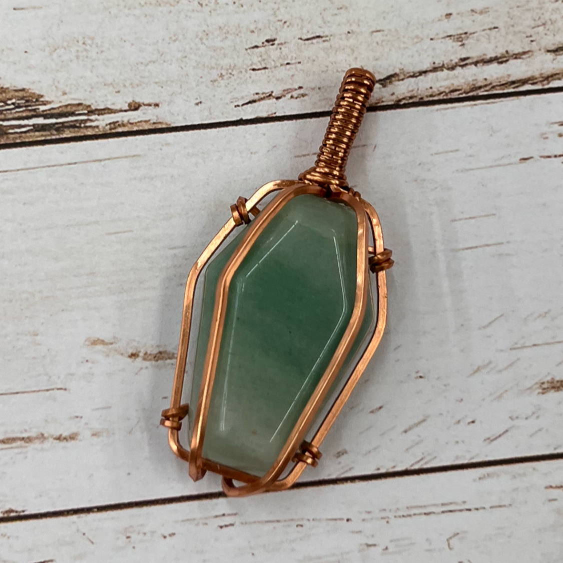 Green coffin shaped stone pendant with copper frame on a wooden surface