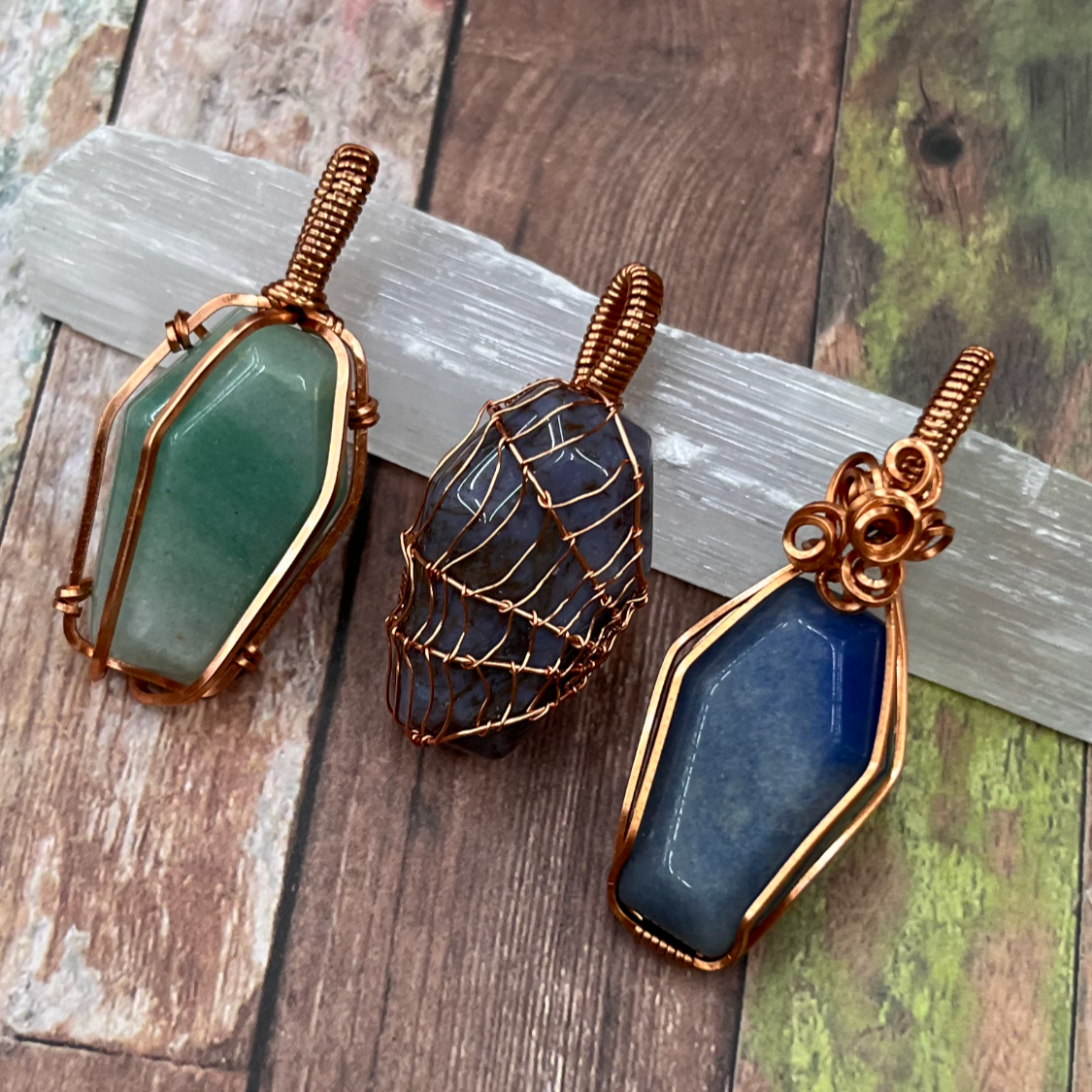 Three wire-wrapped, coffin shaped stone pendants on a wooden surface